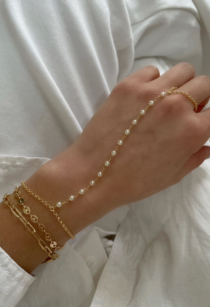 A delicate hand chain featuring a dainty cable bracelet and a single pearl that loops onto your middle finger. Lightweight, elegant, and effortlessly romantic.