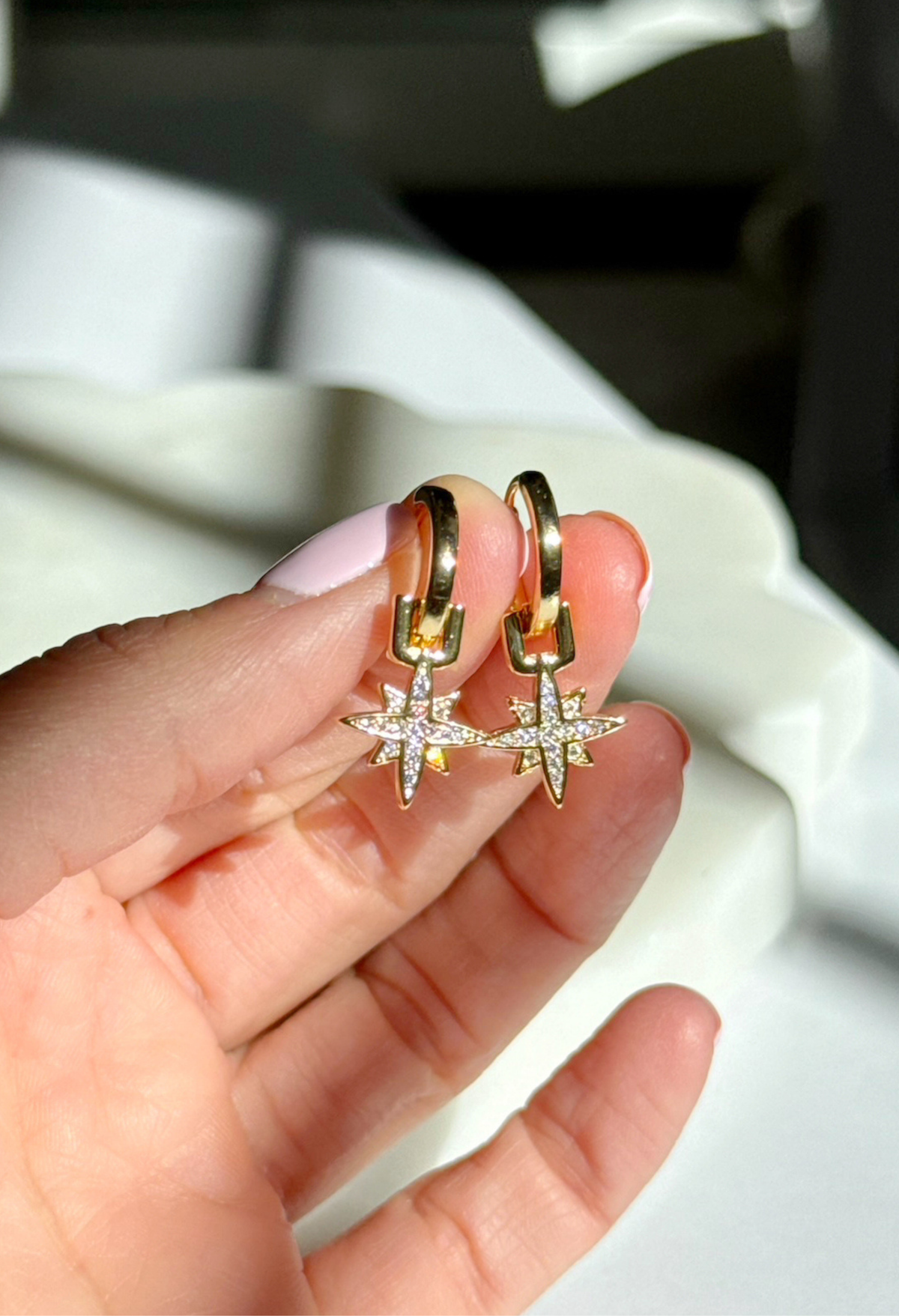 Gold hoop earrings with star designs held in a hand against a blurred background